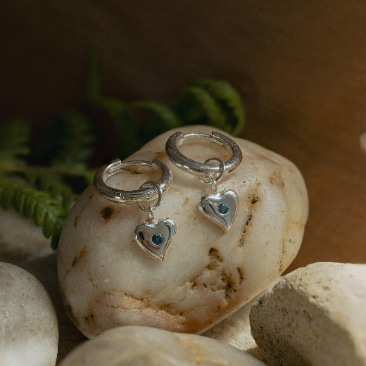 Silver hoop earrings with heart charms on a stone surface