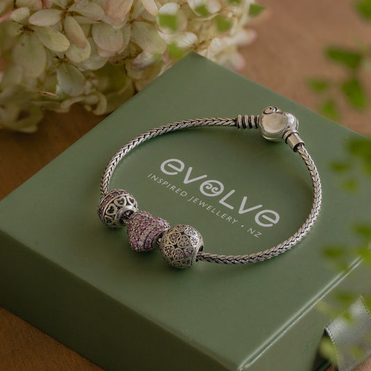 Silver bracelet with charms on a green box labeled 'Evolve Inspired Jewellery NZ'.
