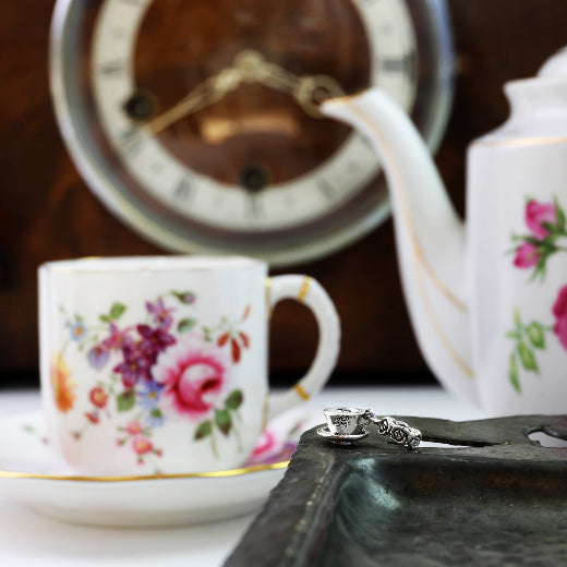 Floral teacup and teapot with a vintage clock in the background and tea cup charm