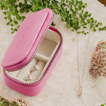 Pink jewelry case with heart-shaped studs on a light background with greenery