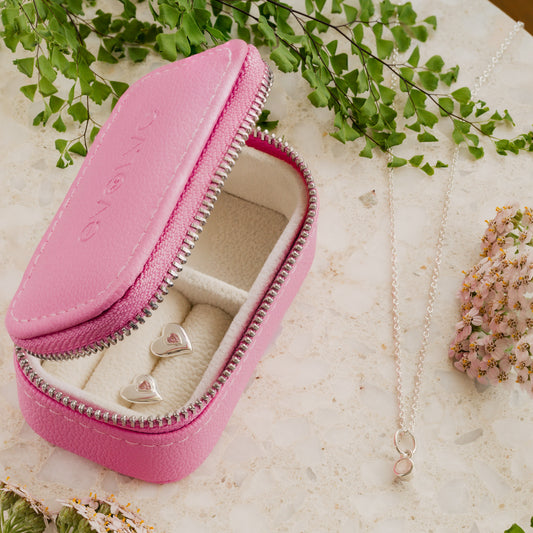 Pink jewelry case with heart-shaped studs on a light background with greenery