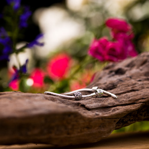 Silver bracelet with Together charm on a stone surface with blurred flowers in the background